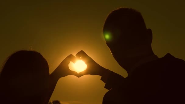 Sun in hand. teamwork of a loving couple. couple in love shows heart symbol with hands. Bride and groom making a heart with their hands against a beautiful sunset on the horizon. happy family concept — Stock Video
