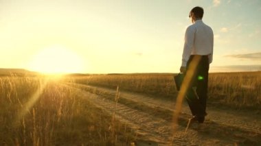 iş adamı elinde bir çanta ile köy yolunda devam ediyor. Girişimci bir kırsal bölgede çalışıyor. gün batımında akşamları toprağını bir çiftçi olup olmadığını denetler. tarıma dayalı işletme kavramı.