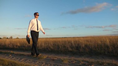 işadamı güneş gözlüğü elinde bir çanta ile ülke yolda gidiyor. tarım iş kavramı. Girişimci bir kırsal bölgede çalışıyor. Çiftçi kara gün batımında olup olmadığını denetler. Ağır çekim