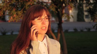 Gözlük ışık takım elbiseli kadınla iş işe gidiyor. kadın güneş ışınları tarafından tarihi bir şehir sokak aşağı yürür ve Smartphone'da konuşuyor.