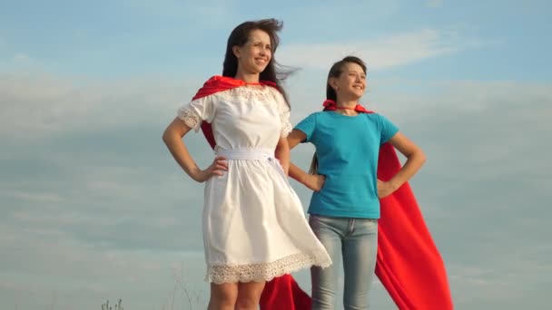 Anya és lánya játszani szuperhősök. két lány piros köpeny szuperhősök áll ellen a kék eget, a szél kinyílásakor egy köpenyt. boldog családi koncepció
