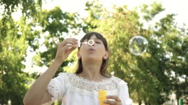 İlkbahar, yaz ve gülümseyen içinde parkta sabun köpüğü üfleme güzel kız. Genç Kız parkta oynarken ve kabarcıklar objektife içine üfleme. Ağır çekim.