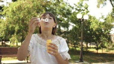 Genç Kız parkta oynarken ve kabarcıklar objektife içine üfleme. Ağır çekim. İlkbahar, yaz ve gülümseyen içinde parkta sabun köpüğü üfleme güzel kız.