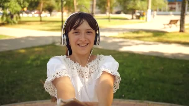 Menina e namorado dançando lado a lado. Movimento lento. menina em fones de ouvido está sorrindo e com telefone dançando e girando com seu amado homem de mãos dadas no parque. trabalho em equipe de um casal amoroso . — Vídeo de Stock