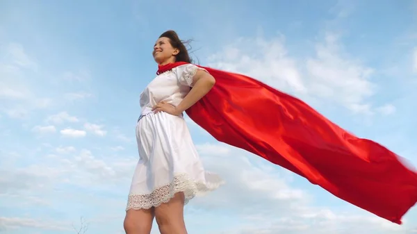 Menina sonha em se tornar um super-herói. sexy super-herói menina de pé no campo em um manto vermelho, vagueando camuflagem no vento. menina em uma expressão de sonho capa vermelha — Fotografia de Stock