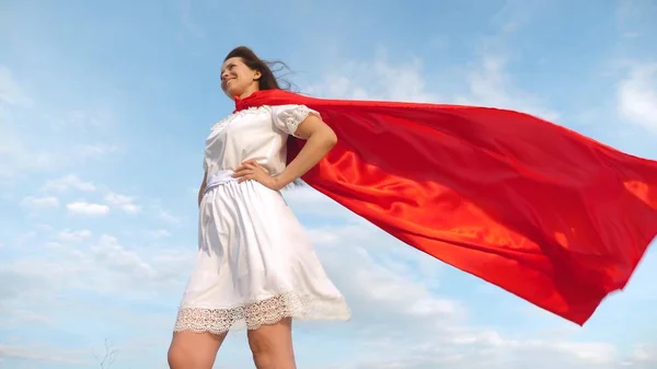 Menina sonha em se tornar um super-herói. sexy super-herói menina de pé no campo em um manto vermelho, vagueando camuflagem no vento. menina em uma expressão de sonho capa vermelha — Fotografia de Stock