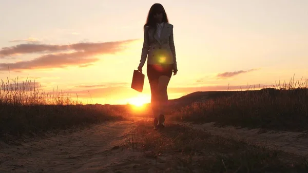 Sexy mujer de negocios caminando a lo largo de un camino de campo con un maletín en la mano, el sol brilla al atardecer. Chica sexy de negocios trabajando en el campo. hermosa chica viaja por el campo . —  Fotos de Stock