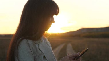 çalışma alanında bulunan sunshine bir tablet ile kadın çiftçi. Kızlar el smartphone ekranında bir mobil ileti yazdırır. Güzel iş kadını bir smartphone perde ile parmak bir günbatımı dokunmadan.
