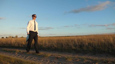 işadamı güneş gözlüğü elinde bir çanta ile ülke yolda gidiyor. tarım iş kavramı. Girişimci bir kırsal bölgede çalışıyor. Çiftçi kara gün batımında olup olmadığını denetler. Ağır çekim