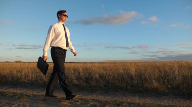 işadamı güneş gözlüğü elinde bir çanta ile ülke yolda gidiyor. tarım iş kavramı. Girişimci bir kırsal bölgede çalışıyor. Çiftçi kara gün batımında olup olmadığını denetler. Ağır çekim