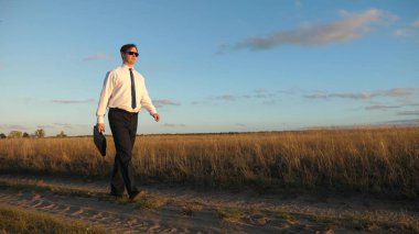 işadamı güneş gözlüğü elinde bir çanta ile ülke yolda gidiyor. tarım iş kavramı. Girişimci bir kırsal bölgede çalışıyor. Çiftçi kara gün batımında olup olmadığını denetler. Ağır çekim