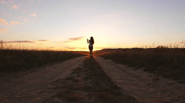 Una donna d'affari cammina lungo una strada di campagna con una tavoletta in mano, il sole miertsaet tra le gambe delle donne. sexy donna d'affari ragazza in esecuzione in campagna. sexy ragazza viaggia in campagna — Foto Stock