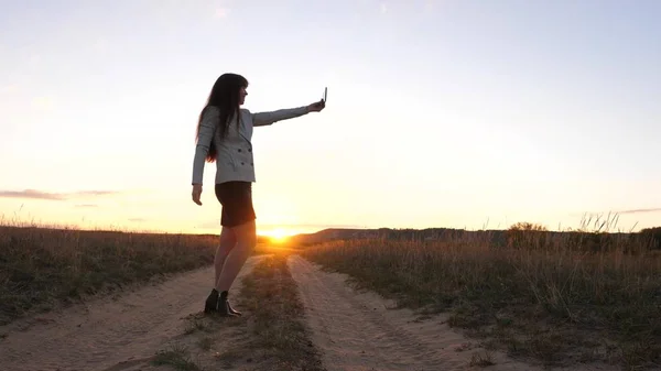 Vacker affärskvinna reser och tar en selfie foto med en mobil smartphone på väg mot solnedgången. begreppet turism. Flicka turist i fältet gör selfie med tablett — Stockfoto