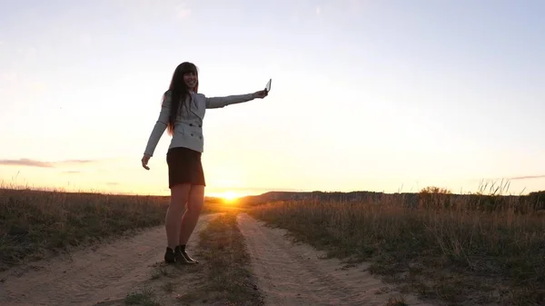 Bella donna d'affari viaggia e scatta una foto selfie utilizzando uno smartphone mobile sulla strada contro il tramonto. concetto di turismo. Ragazza turista nel campo fa selfie con tablet — Foto Stock