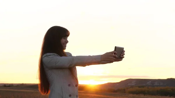 Flicka turist i fältet gör selfie med tablett. vacker affärskvinna reser och tar en selfie foto med en mobil smartphone mot bakgrund av solnedgången. begreppet turism — Stockfoto