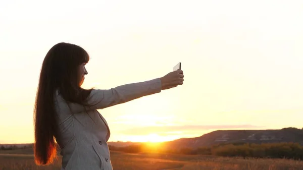 Flicka turist i fältet gör selfie med tablett. vacker affärskvinna reser och tar en selfie foto med en mobil smartphone mot bakgrund av solnedgången. begreppet turism — Stockfoto