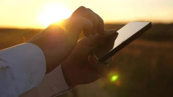 hands of man are driving their fingers over tablet. man checks email. Businessman working on tablet at sunset in park. agronomist works with the tablet in the field. farmer on plantation with