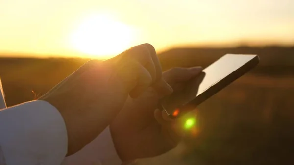 hands of man are driving their fingers over tablet. man checks email. Businessman working on tablet at sunset in park. agronomist works with the tablet in the field. farmer on plantation with