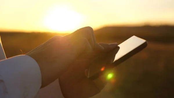 hands of man are driving their fingers over tablet. man checks email. Businessman working on tablet at sunset in park. agronomist works with the tablet in the field. farmer on plantation with