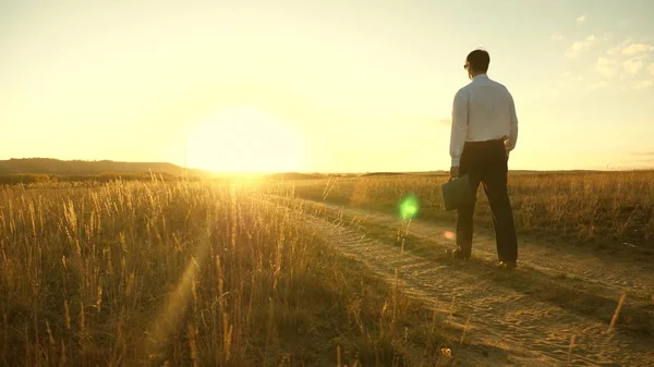iş adamı elinde bir çanta ile köy yolunda devam ediyor. Girişimci bir kırsal bölgede çalışıyor. gün batımında akşamları toprağını bir çiftçi olup olmadığını denetler. tarıma dayalı işletme kavramı.