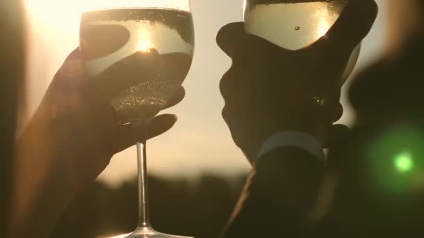 シャンパンの輝きと太陽の下で発泡体。夕日の背景にスパーク リング ワインとワイングラスを持って愛のカップル。クローズ アップ。愛するカップルのチームワーク。成功と勝利を祝います。スローモーション — ストック動画