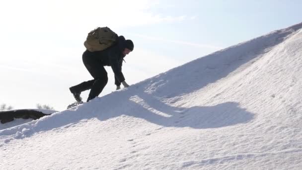 Alpinista człowiek przesuwa się do góry do jego sukcesu. Wspinacz wspina się po zaśnieżonej górskiej w promienie słoneczne. podróżny raduje się w jego zwycięstwo i podnosi ręce przed niebo na szczycie góry — Wideo stockowe