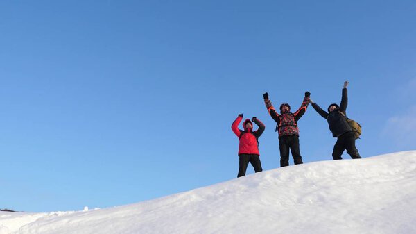 Travelers come to the top of a snowy hill and enjoy the victory against the blue sky. teamwork and victory. teamwork of people in difficult conditions. tourists travel in the snow in winter.