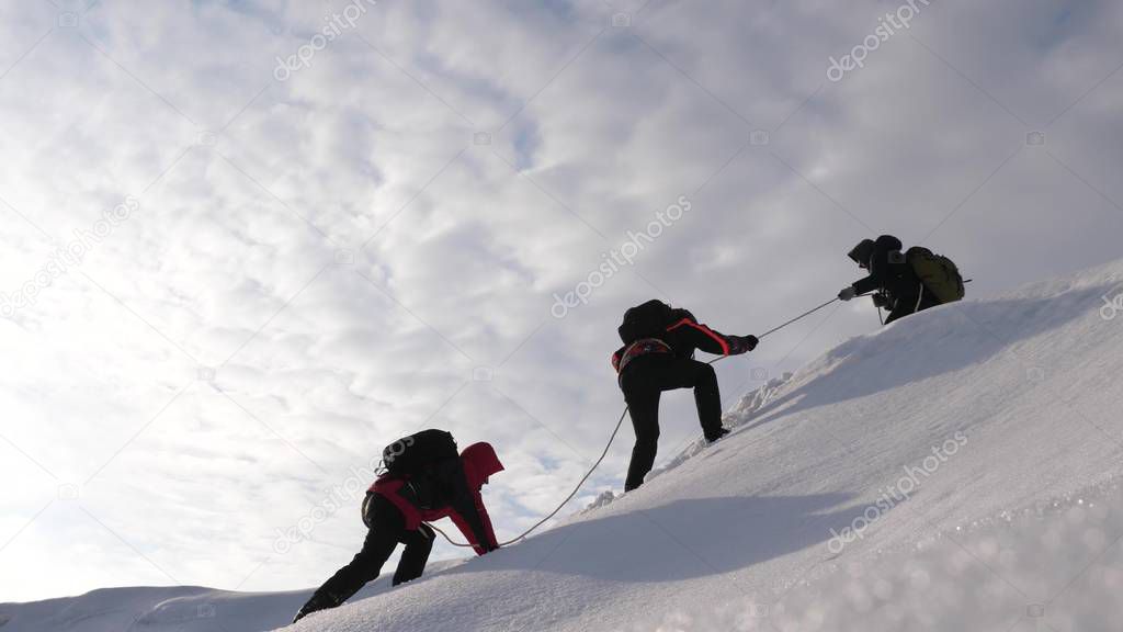 three Alpenists in winter climb rope on mountain. Travelers climb rope to their victory through snow uphill in a strong wind. tourists in winter work together as team overcoming difficulties.