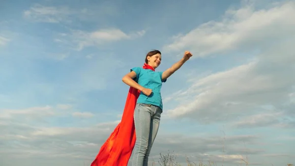 Девушка мечтает стать супергероем. Молодая девушка, стоящая в красном плаще, выражая свои мечты. красивая девушка супергерой стоит на поле в красном плаще, плащ развевается на ветру. Медленное движение — стоковое фото