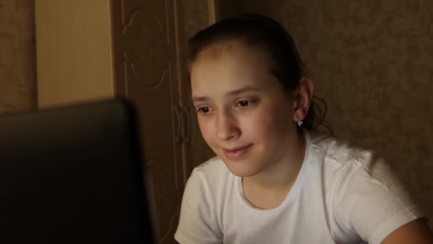 Boldog tini lány játszik a laptopon. Egy fiatal lány néz egy számítógép képernyőjén, és mosolyog a szobájában éjjel. lány hallgató készül, hogy tanulmányozza a laptop otthon a szobában. — Stock videók