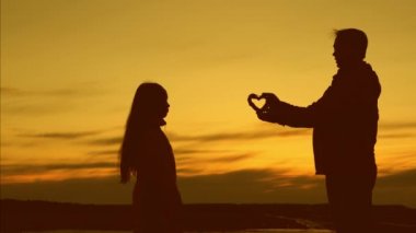 Babam küçük kızına gün batımında kalp sembolü veriyor. mutlu aile kavramı. seven baba küçük bir kızın siluetini uzatır. Baba oynuyor ile onun kız.