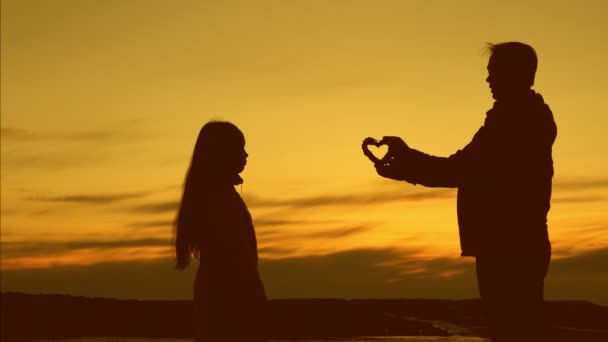 Tata daje swoją małą córkę symbol serca o zachodzie słońca. szczęśliwej koncepcji rodzinnej. kochający Ojciec rozciąga sylwetkę małej dziewczynki. Tata gra z córką. — Wideo stockowe