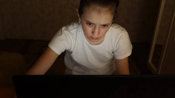 Chica adolescente cansado mira en la pantalla de un monitor portátil. Primer plano. Una joven mira a la pantalla del ordenador con los ojos cansados en su habitación por la noche. chica adolescente cansado mira en la pantalla de un monitor portátil . — Foto de Stock