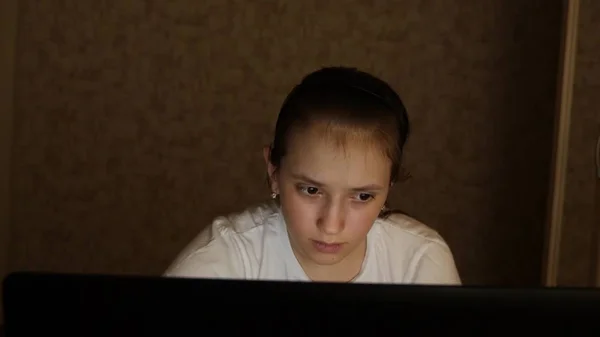 Vermoeid tiener meisje kijkt in het scherm van een laptop monitor. Close-up. Een jong meisje kijkt naar computerscherm met vermoeide ogen in haar kamer 's nachts. vermoeid tiener meisje kijkt in het scherm van een laptop monitor. — Stockfoto