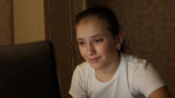 Chica adolescente feliz jugando juegos en el ordenador portátil. Una joven mira la pantalla de una computadora y sonríe en su habitación por la noche. estudiante chica se prepara para estudiar para el ordenador portátil en casa en la habitación . — Foto de Stock