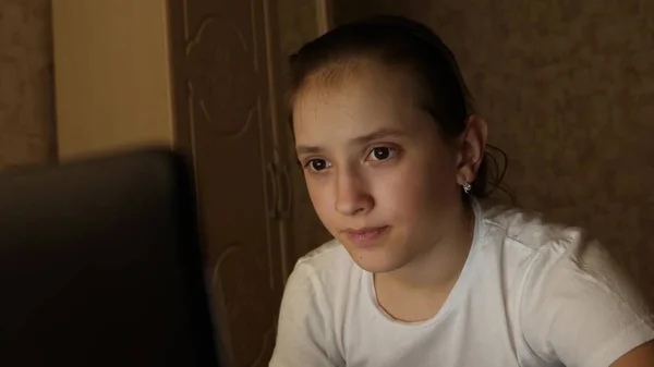 Chica adolescente feliz jugando juegos en el ordenador portátil. Una joven mira la pantalla de una computadora y sonríe en su habitación por la noche. estudiante chica se prepara para estudiar para el ordenador portátil en casa en la habitación . — Foto de Stock