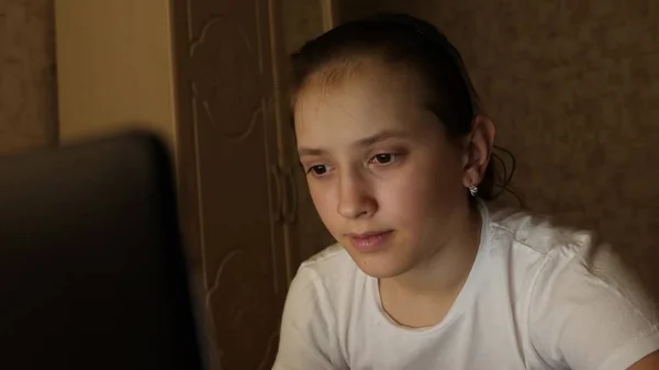 Chica adolescente feliz jugando juegos en el ordenador portátil. Una joven mira la pantalla de una computadora y sonríe en su habitación por la noche. estudiante chica se prepara para estudiar para el ordenador portátil en casa en la habitación . — Foto de Stock