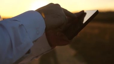 Parkta gün batımında tablette çalışan bir işadamı. adamın elleri tabletin üzerinde parmaklarını sürüyor. adam e-posta denetler. agronomist alanında tablet ile çalışır. akıllı telefon ile tarlasında çiftçi.