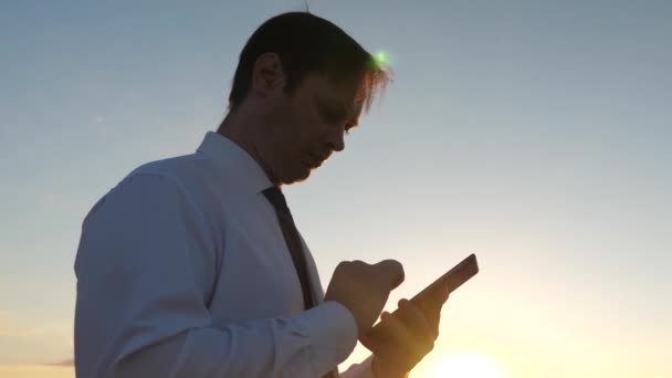 Mann in Krawatte mit Tablet und E-Mail checken im Park bei Sonnenuntergang. Geschäftsmann arbeitet mit Tablet, Smartphone gegen Himmel. Handy-Nachricht auf Smartphone-Bildschirm. Geschäftsmann auf Landstraße mit Navigator — Stockvideo