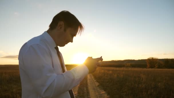 Hombre de negocios jugando juegos de tableta en el parque en los cálidos rayos de la puesta de sol. hombre jugando juegos en el teléfono inteligente. hombre feliz en camisa blanca y corbata juega en línea en la tableta . — Vídeo de stock