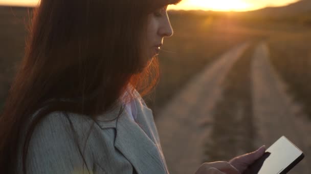 Agricultora que trabaja con una tableta en el campo a la luz del sol. Hermosa mujer de negocios tocando la pantalla de un smartphone con los dedos de una puesta de sol. niñas manos imprime un mensaje móvil en la pantalla del teléfono inteligente . — Vídeo de stock