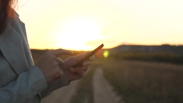 Agricultora que trabaja con una tableta en el campo a la luz del sol. Hermosa mujer de negocios tocando la pantalla de un smartphone con los dedos de una puesta de sol. niñas manos imprime un mensaje móvil en la pantalla del teléfono inteligente . — Vídeo de stock