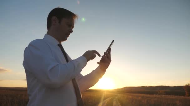 Mains de l'homme conduisent leurs doigts sur la tablette. homme vérifie email. Homme d'affaires travaillant sur tablette au coucher du soleil dans le parc. agronome travaille avec la tablette dans le domaine. agriculteur sur plantation avec — Video