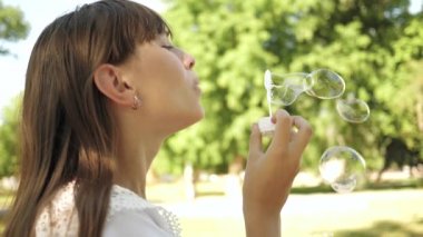Güzel kız bahar, yaz ve gülümseyen parkta sabun kabarcıklar üfleme. Close. Parkta oynayan genç kız ve kabarcıklar yakın çekim üfleme. Yavaş hareket.