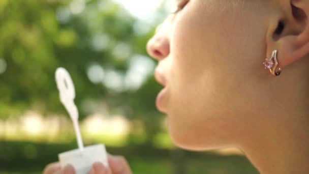 Güzel kız bahar, yaz ve gülümseyen parkta sabun kabarcıklar üfleme. Genç kız üfleme sabun kabarcıklar yakın çekim. Yavaş hareket. — Stok video