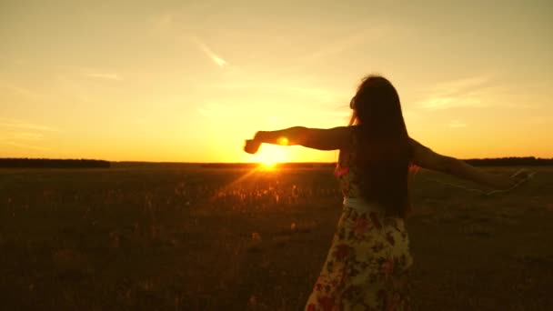 Menina feliz ouvir música e dançar nos raios de um belo pôr do sol no parque. jovem menina em fones de ouvido e com um giro smartphone em voo sob os raios de um pôr do sol quente . — Vídeo de Stock