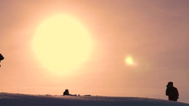 Tourists come to top of snowy hill and rejoice at victory against backdrop of a yellow sunset. travelers met on top of success. teamwork and victory. ecological tourism — Stock Video