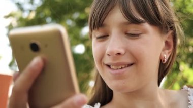 Güzel kız akıllı telefonda İlkbahar, yaz yakın çekim parkta bir mektup yazıyor. kız arkadaşlarınızla tablet sohbet. Genç kız tezgah üzerinde Smartphone fotoğrafları üzerinden bakar. Online e-posta kontrol.