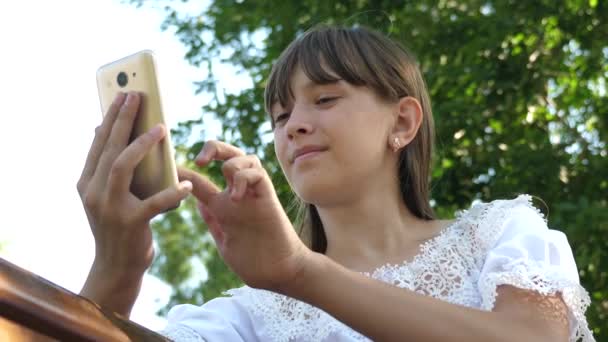 美しい少女は、スマートフォンに春、夏に公園で手紙を書く。若い女の子が友人とタブレットでチャット。十代の少女は、ベンチにスマートフォンで写真を見て。オンラインでメールをチェック. — ストック動画