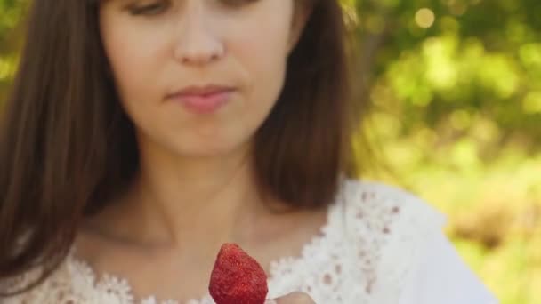 Lycklig Tjej äter jordgubbar på sommaren i trädgården. Läcker jordgubbs dessert. vacker flicka äter röd jordgubb från en kopp och leenden. Vitamin-och bär diet för kvinnor. — Stockvideo
